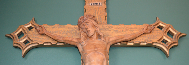 Torso and outstretched arms of wooden Christ on a wooden crucifix against a teal background