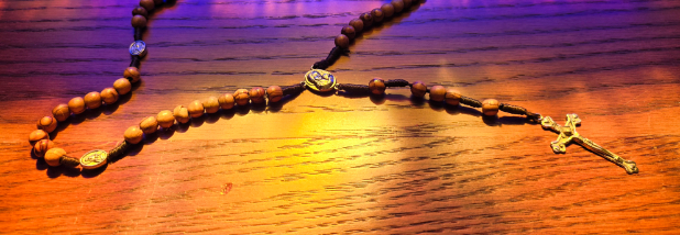 Wooden rosary beads on wooden table with stained glass reflection