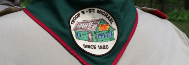 Green neckerchief with patch of green cabin and words Troop 9 St. Michael Since 1920, against the back of a tan uniform