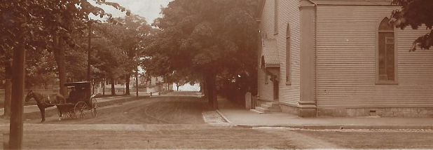 Sepia-toned photo of dirt intersection with a horse-drawn carriage and church
