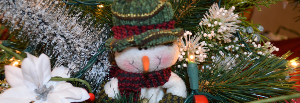 Snowman ornament on Christmas tree with white lights and white flower